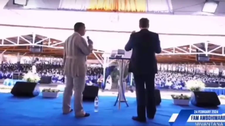two men standing with microphones on a stage in front of a large crowd