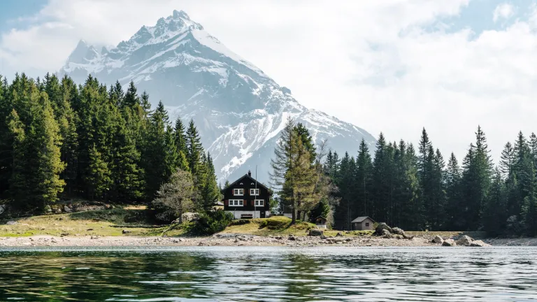 Photo of cabin on a lake with mountains in the distance.