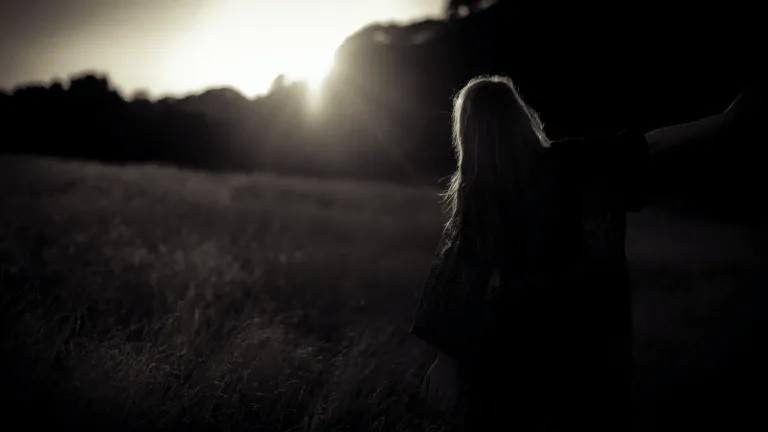 A woman sitting in a field while the sun is setting.