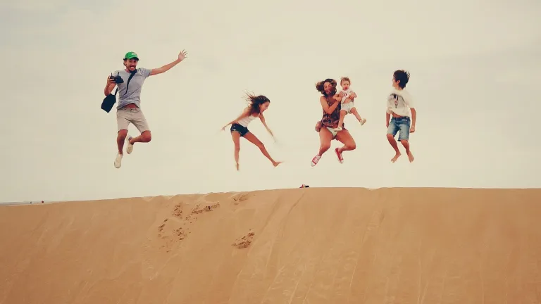 A family jumping up from a sand dune.