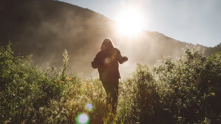 Photo of person hiking forward towards sunlight.