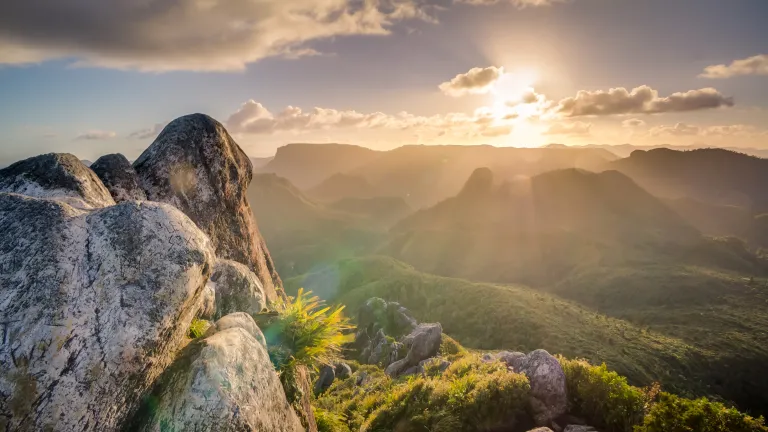 Photo of the sun shining over a mountain.