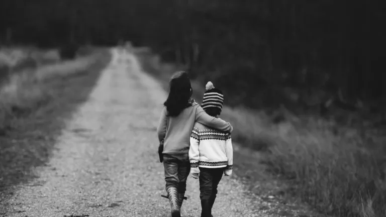 Black and white photo of two children walking down a road, each with an arm around the other's shoulders.