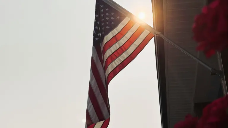 A photo of the American flag with the sun rising behind it.