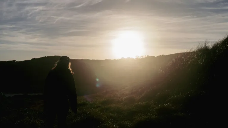 A bright sunset going down over a hill with a person in the foreground.