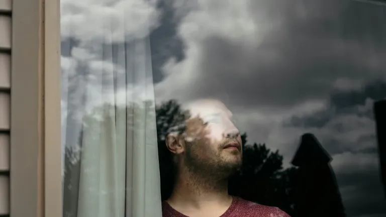 Man looking out window with gloomy clouds in the sky