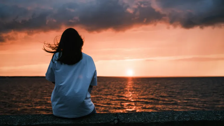 Living as citizens of God’s Kingdom begins now, as we submit to Christ’s rule today and look forward to His eternal reign tomorrow. A woman sitting by a body of water watching the sunset.