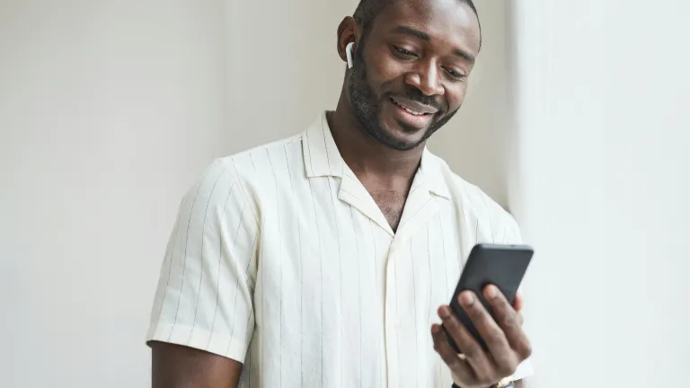 a man holding a phone and wearing earbuds while standing indoors