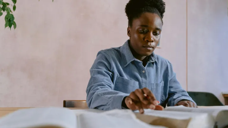 a woman sitting at a table and looking at two open Bibles