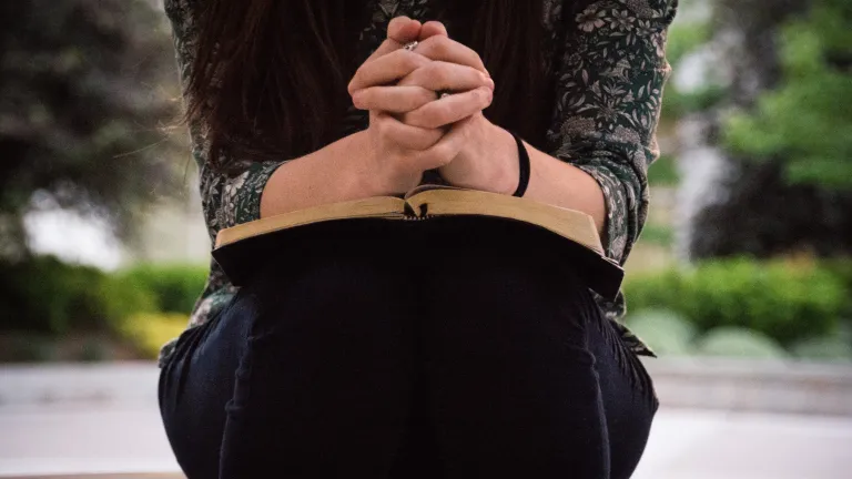 A woman with her arms resting on an open Bible.