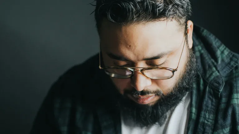 A man with a beard and wearing glasses has his head bowed.