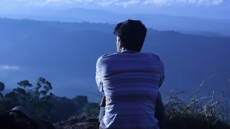 a man sitting on a hill and looking out over a blue horizon