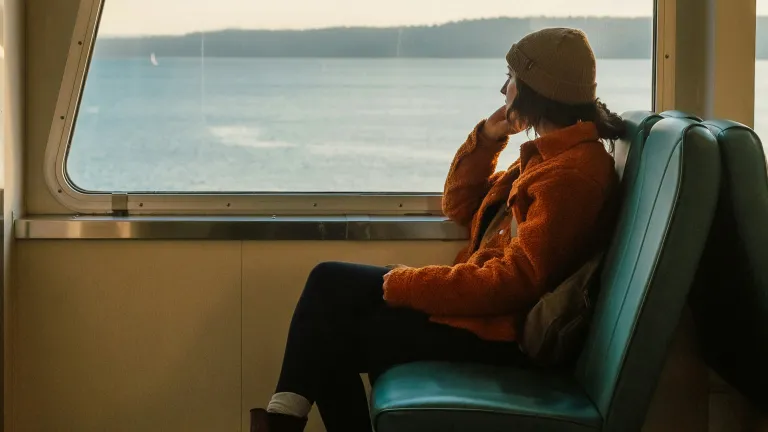 a woman sitting on a bus and looking out the window at a lake
