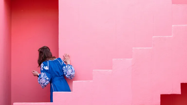 a woman looking through a doorway in the midst of two pink staircases
