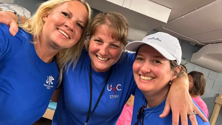Three women wearing United Youth Camp shirts smiling