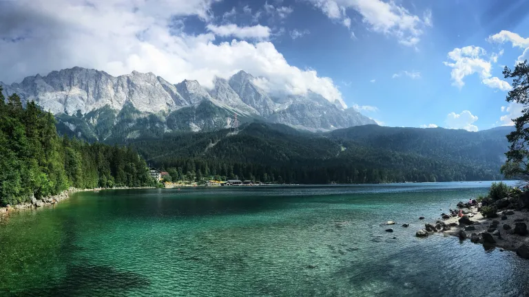 a lake surrounded by trees and mountains with a cloudy sky overhead