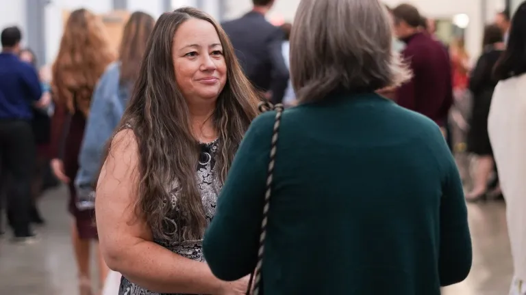 two women talking in a room full of people