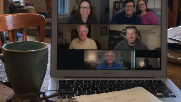 a laptop with a video call open and a coffee mug and notebook on a desk