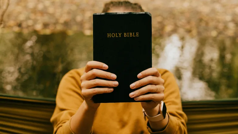 Person holding a Bible in front of their face