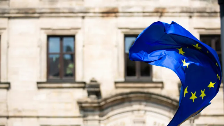 A European Flag blowing in the wind outside of an old building.