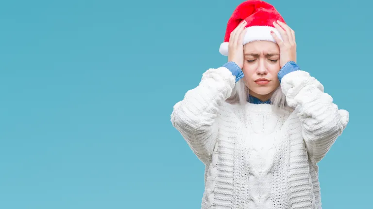 A woman wearing a santa claus hat grabbing her head as if she is frustrated.