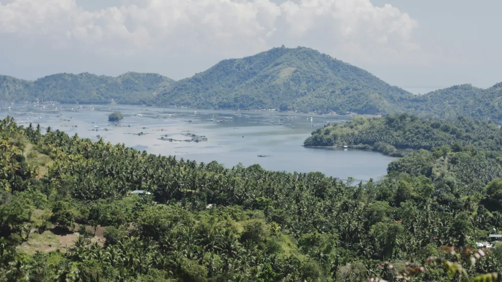 green hills surrounding a pale blue body of water with clouds overhead