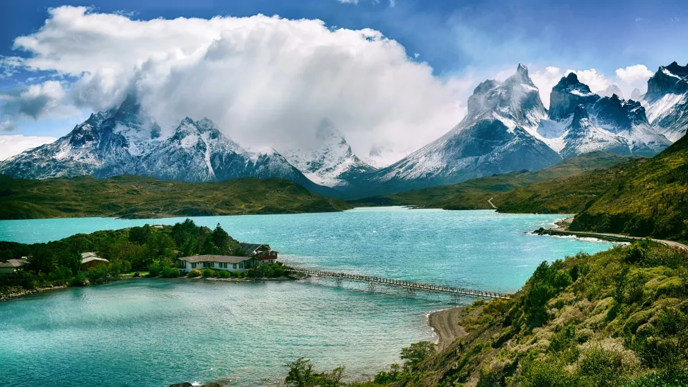 a blue lake surrounded by mountains with an island, accessed by a bridge, in the center