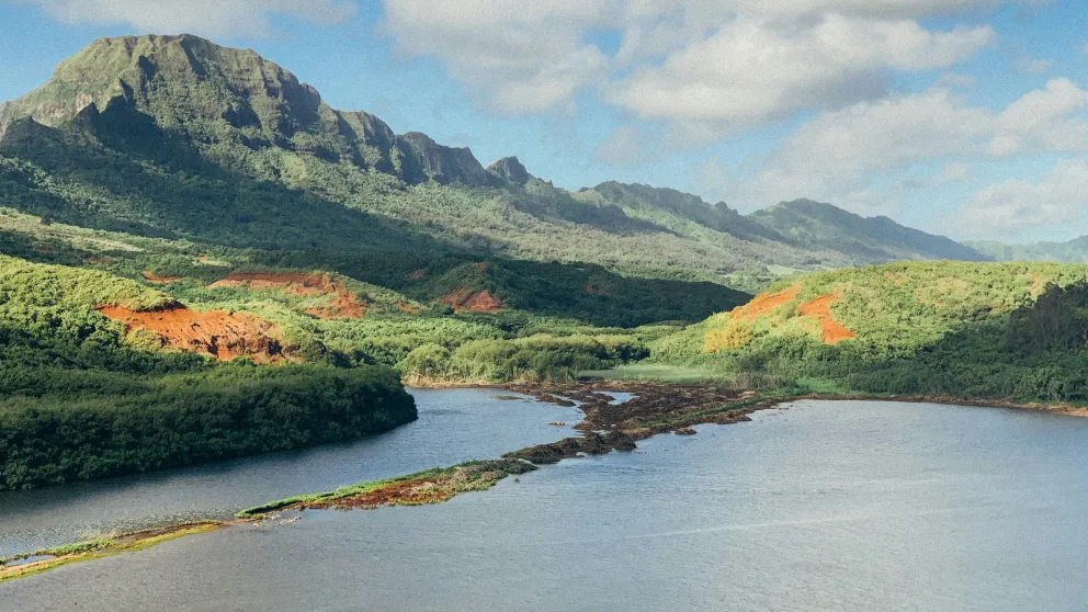 green mountains beside river under white clouds and blue sky during daytime