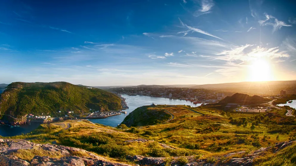 rolling green and gold hills surrounding a small body of water with the sun shining just at the horizon