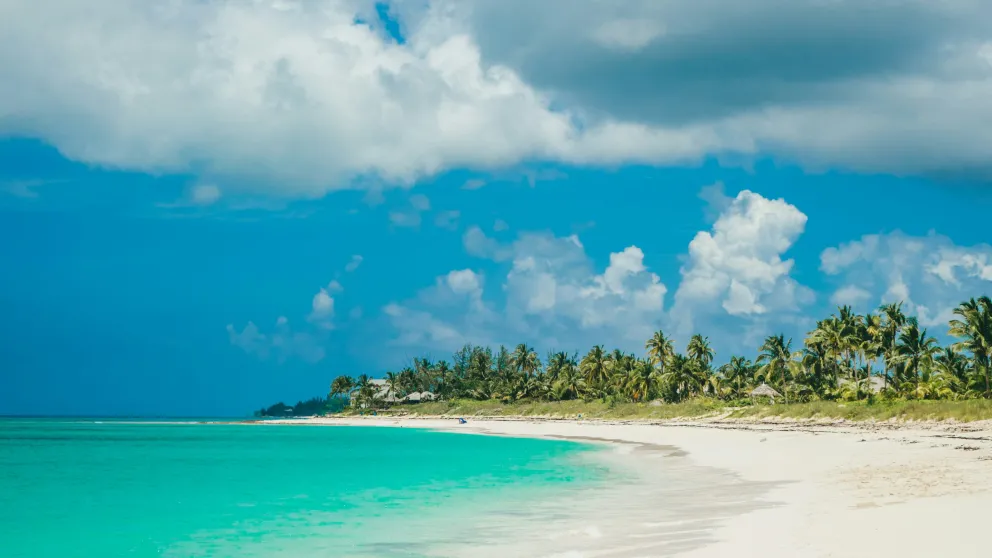 a beach with with white sand and bright blue water under a blue sky full of fluffy clouds