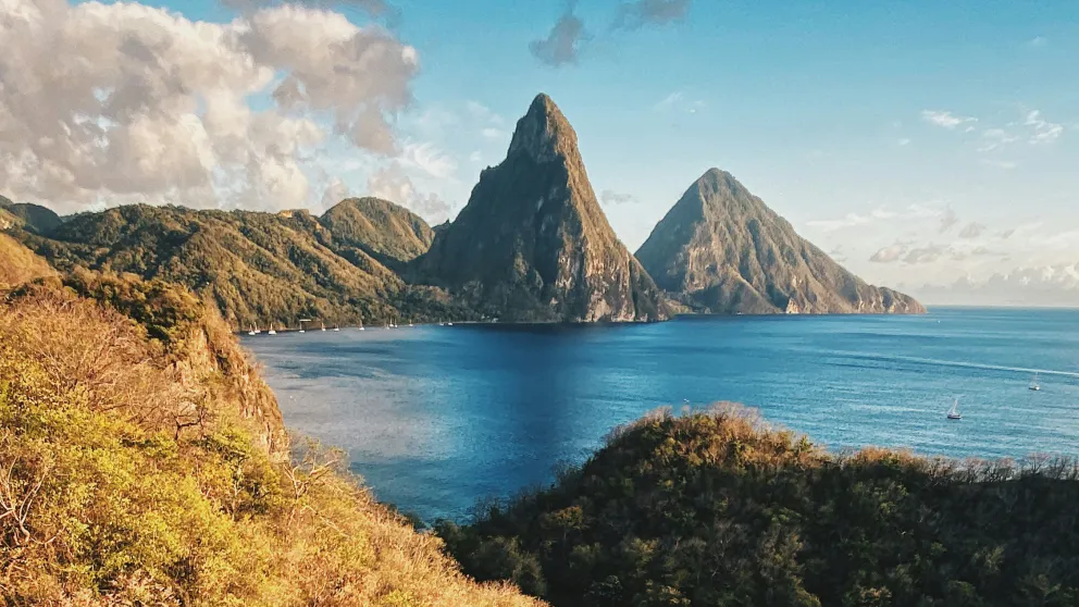 twin piton mountains under a cloudy sky with a body of water in the foreground