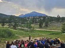 Campers gathered for campfire with a mountain range in the background