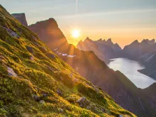 a mountainside with the sunset peeking through the horizon