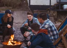 three men and a woman sitting around a campfire