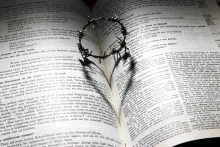 a crown of thorns casting a heart-shaped shadow on a Bible opened to a passage about Christ