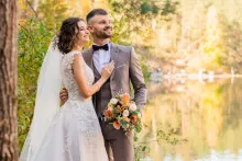 a man and a woman in wedding attire outdoors with a lake in the background