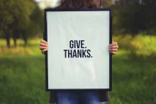 A person holding a sign that says: Give. Thanks.