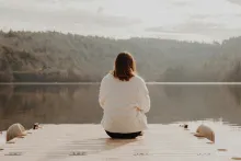 A woman sitting on a dock looking out over a lake.