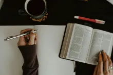 A woman writing notes with a Bible open.
