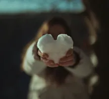 a pair of hands holding a heart made of snow
