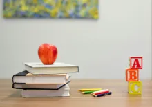 an apple on a stack of books, a few colored pencils and a stack of ABC blocks on a wooden desk