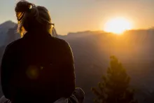 A person looking at the sun going down over a mountain.