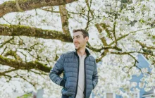 a man walking underneath tree branches covered in white blossoms