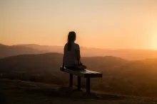 A young woman sitting on a bench looking out over a vista of rolling hills.