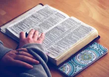 A woman with an open Bible laying on a table.
