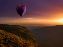 a hot air balloon flying over a hilly landscape at sunset