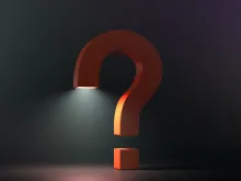 a 3-D orange question mark standing on the floor against a dark background