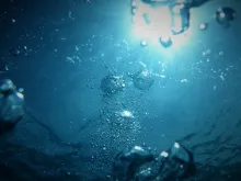 a view from underwater looking up towards the surface where sunlight hits the water, highlighting the bubbles underwater