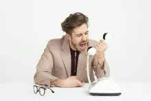 an angry man yelling into the receiver of a phone