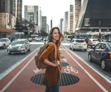 a smiling woman with a backpack standing in the middle of a road in a city